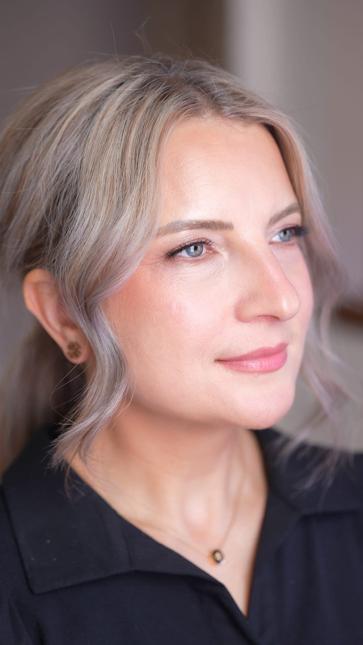 Close-up three-quarter portrait of a client wearing a soft, natural glam look — luminous skin, a softly blended neutral eye, warm blush, and a glossy pink lip.
